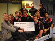Picture shows Jim Lang from CHAS, on the rowing machine, receiving the cheque from Richard Sawyer - who is holding the cheque just on the right of Jim - and Boat Club members